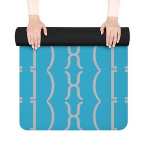 May include: A rolled-up yoga mat with a black exterior and a blue patterned interior. The pattern features a repeating design of light gray curved shapes and vertical lines. The mat is unrolled, revealing the blue surface.