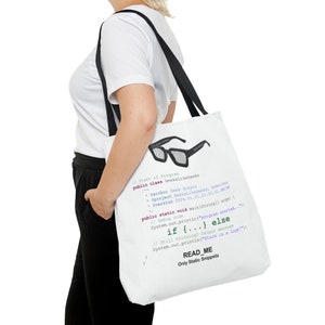 Puede incluir: Una bolsa de tela blanca con asas negras presenta un gráfico de unas gafas negras con código impreso en la bolsa. El código dice "//Start of Program public class GeeksLikeGeeks ... if {...} else ... READ_ME Only Static Snippets".