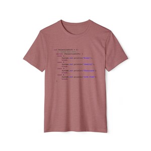 Pode incluir: Uma camiseta rosa claro com um trecho de código impresso nela. O código é escrito em Java e inclui o texto "int ValentineGift = 2;" e "System.out.println("Love Poem");".