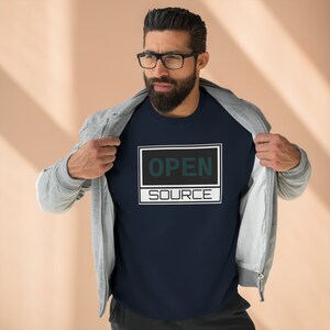 May include: Navy blue crew neck sweatshirt with the words "OPEN SOURCE" in a white and black rectangular design. The text "OPEN" is in dark green. The sweatshirt is being revealed by a person wearing a gray zip-up hoodie.