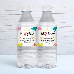 May include: Two clear plastic water bottles with colourful labels that say "hi five let's celebrate Maggie's 5th birthday!" The labels have a handprint, paint splatters, and a sun graphic.
