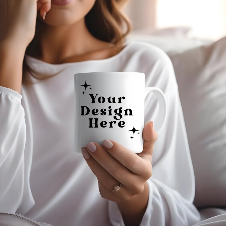 May include: White ceramic mug with black text that reads "Your Design Here" and two small stars on either side of the text. The mug is being held by a person.