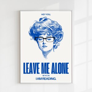 Könnte beinhalten: Ein blaues und weißes Poster mit einer Zeichnung einer Frau, die eine Brille trägt, und dem Text "HEY YOU, LEAVE ME ALONE WHEN I AM READING."