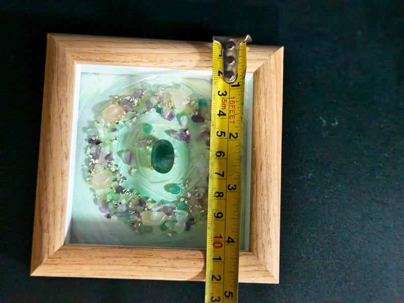 Pu&ograve; includere: Un'opera d'arte incorniciata con una pietra verde centrale circondata da un motivo a spirale e varie pietre preziose. La cornice &egrave; in legno chiaro. L'opera misura circa 7,6 cm di altezza.