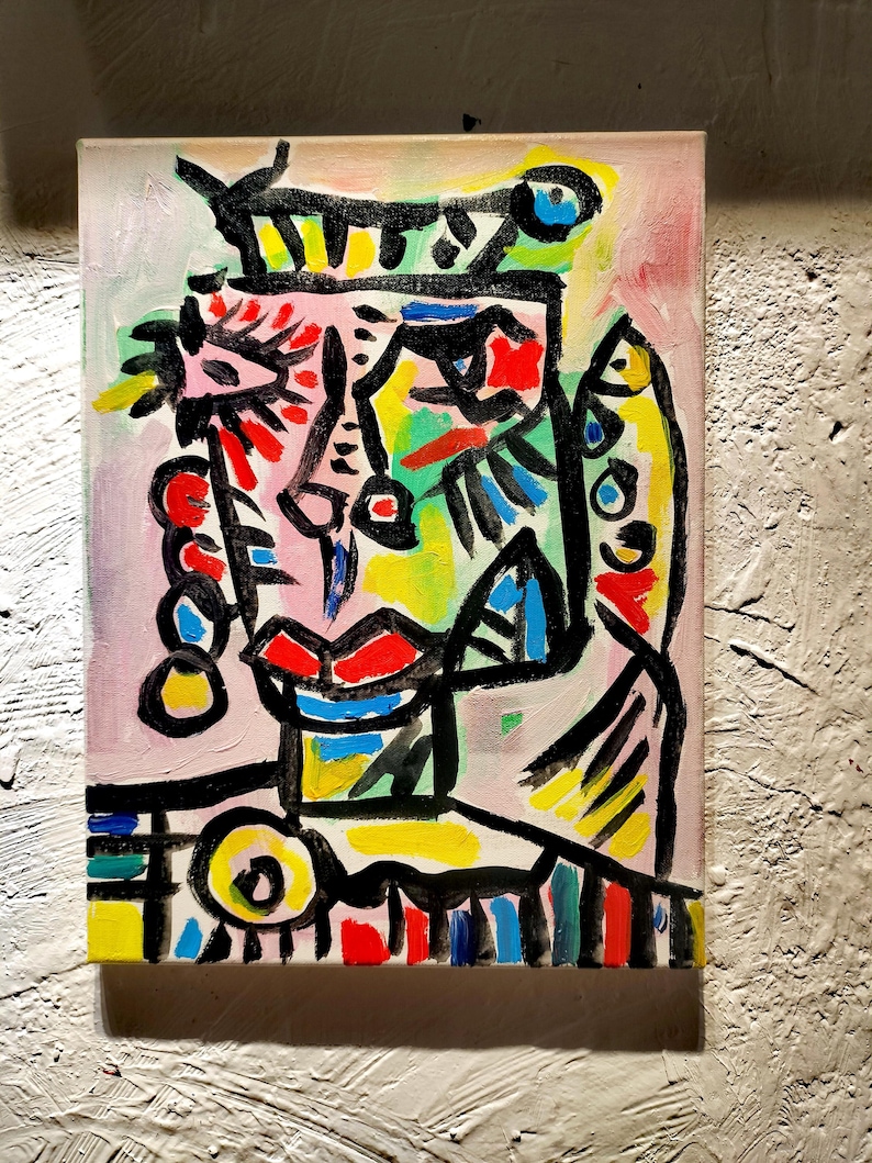 Puede incluir: Pintura abstracta de una cara con l&iacute;neas negras audaces, colores brillantes y una corona. La cara est&aacute; pintada en tonos de rosa, rojo, amarillo, verde y azul.