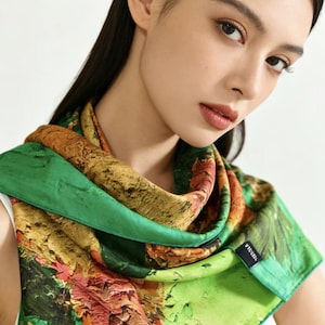 May include: A silk scarf featuring an abstract design in green, orange, and brown hues. The scarf is draped around the neck, highlighting its colourful pattern and soft texture. The scarf has a label that says "VISSLA".