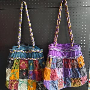 Puede incluir: Dos bolsos tote de patchwork con asas trenzadas. Un bolso es azul, el otro es morado. Ambos bolsos tienen un diseño de patchwork con detalles bordados en varios colores, incluyendo naranja, verde y rojo.