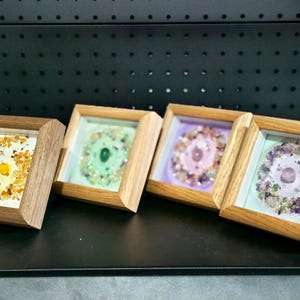 Pu&ograve; includere: Quattro opere d'arte incorniciate con cornici in legno. Ogni pezzo presenta una disposizione circolare di pietre preziose colorate. Le pietre preziose sono gialle, verdi, rosa e viola. Le cornici sono esposte su una superficie nera.