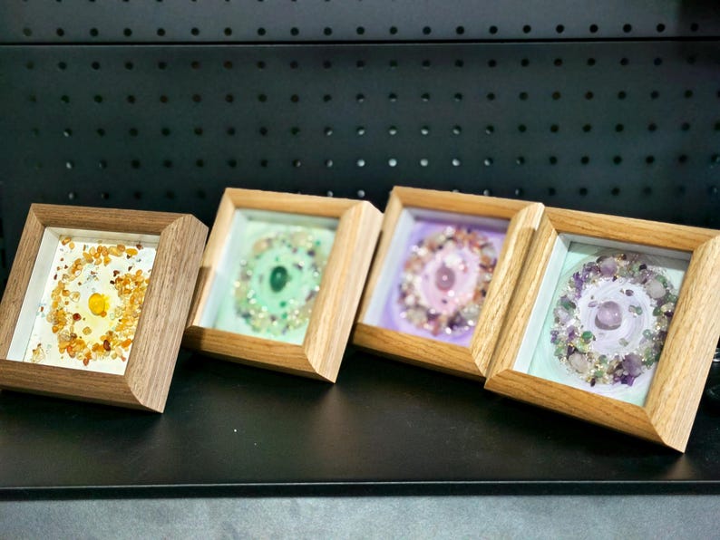 Pu&ograve; includere: Quattro opere d'arte incorniciate con cornici in legno. Ogni pezzo presenta una disposizione circolare di pietre preziose colorate. Le pietre preziose sono gialle, verdi, rosa e viola. Le cornici sono esposte su una superficie nera.
