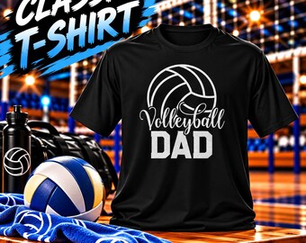 May include: A black short-sleeved t-shirt featuring a white graphic of a volleyball and the text "Volleyball DAD". The shirt is displayed alongside a blue and white volleyball, a black water bottle with a volleyball icon, and a blue towel.