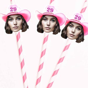 May include: Three pink and white striped paper straws with pink cowboy hats and the number 29 on them. The hats have a sparkly pink design.