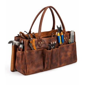 May include: A brown leather tool bag with multiple pockets and a handle. The bag is filled with various tools, including a hammer, pliers, and screwdrivers. The leather has a distressed look.