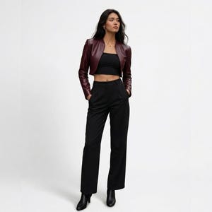 Full-length studio photo of a model wearing the burgundy leather cropped jacket, black crop top, and black pants against a white background.