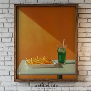 Può includere: Una stampa incorniciata di una natura morta con un bicchiere di liquido verde con una cannuccia e un piatto di patatine fritte su un tavolo bianco su sfondo giallo. La stampa è intitolata "a stiller life" con il testo "art print collection" sotto il titolo.