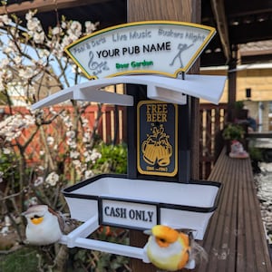 Puede incluir: Un letrero decorativo de pub con el texto "YOUR PUB NAME" y "Beer Garden". El letrero incluye un gráfico de "FREE BEER" y un letrero de "CASH ONLY". Dos figuras de pájaros están posadas en el letrero.