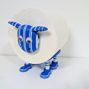 May include: A whimsical toilet paper holder shaped like a sheep. The sheep's head and legs are blue with white stripes, and it has googly eyes. The body is a roll of white toilet paper, creating a fun and functional bathroom accessory.