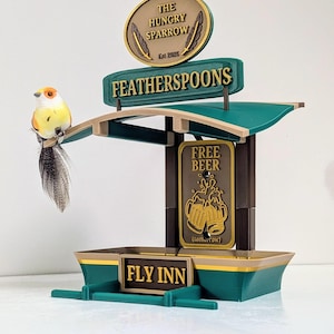 Puede incluir: Un letrero caprichoso de varios niveles para un negocio llamado "Fly Inn" y "The Hungry Sparrow". El letrero es de color verde azulado, marrón y dorado, con las palabras "Featherspoons" y "Free Beer" mostradas. Un pájaro decorativo se posa en el letrero.