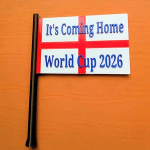 May include: A white rectangular flag with a red cross, featuring the blue raised text It's Coming Home and World Cup 2026. The flag is attached to a black pole on the left side, displaying a clear design for sports fans and event supporters.