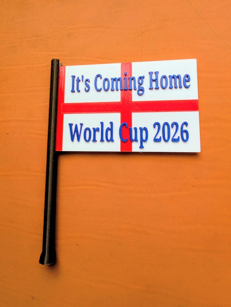 May include: A white rectangular flag with a red cross, featuring the blue raised text It's Coming Home and World Cup 2026. The flag is attached to a black pole on the left side, displaying a clear design for sports fans and event supporters.