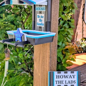 May include: A black, white, and light blue bird feeder featuring the text Howay The Mags, Newcastle We Are The Geordies, and Fly Thru. A separate rectangular sign displays the text Howay The Lads Newcastle in black, white, and light blue.