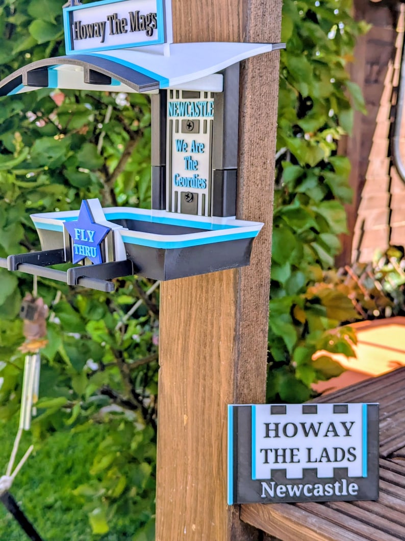 May include: A black, white, and light blue bird feeder featuring the text Howay The Mags, Newcastle We Are The Geordies, and Fly Thru. A separate rectangular sign displays the text Howay The Lads Newcastle in black, white, and light blue.
