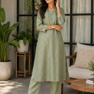 May include: A sage green kurta set featuring a long-sleeved tunic with a subtle gold scalloped pattern and a notched neckline, paired with matching straight-leg trousers. The ensemble is crafted in a solid light green tone with gold embroidery.