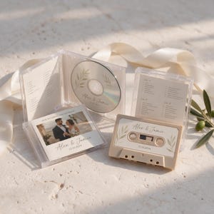 May include: A clear plastic CD case containing a disc with leaf illustrations and the text Alex & Jamie 12.10.2024, alongside a matching beige cassette tape and a printed insert featuring a photograph of a couple and the text Our Wedding Soundtrack.