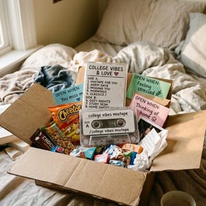 Peut inclure: Une boîte en carton ouverte remplie de collations, de bonbons et d'une cassette audio intitulée "college vibes mixtape". La boîte contient également de petits papiers avec des phrases comme "Open When: Feeling stressed". La boîte est sur un lit.