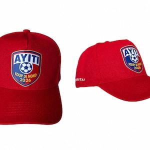 Può includere: Un cappellino da baseball rosso brillante con uno stemma a forma di scudo sul davanti. Lo stemma mostra il testo AYITI, un grafico di un pallone da calcio e le parole KOUP DI MOND 2026. Il lato del cappellino riporta la parola HERITAJ in bianco.
