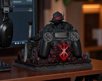 Puede incluir: Soporte negro para mando con una figura de guerrero con espada, mando y emblema rojo. El soporte está sobre una base oscura con un diseño texturizado detallado. La figura lleva un casco con ojos rojos brillantes.