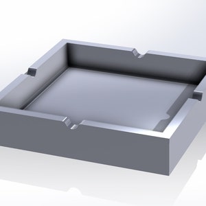 May include: A silver metal ashtray with a square shape and rounded corners. The ashtray has four sides and a rectangular opening in the centre.