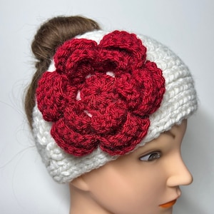 Puede incluir: Diadema de punto blanco con una gran flor roja de ganchillo en la parte superior. La diadema está diseñada para llevarse con una coleta.