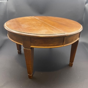 May include: A small, round wooden table with a dark brown finish. The table has a circular top and four short, square legs. The top appears to be made of two pieces of wood joined together. The table is approximately 46 cm in diameter.