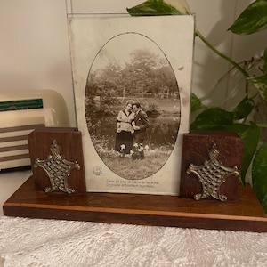 May include: A vintage wooden picture frame with an oval photograph of a couple. The frame has two decorative metal accents and a wooden base. The photograph is in black and white.