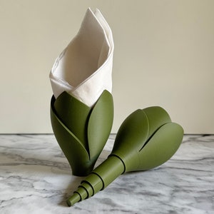 May include: Two green flower-shaped napkin holders. One holder has a white napkin inside.