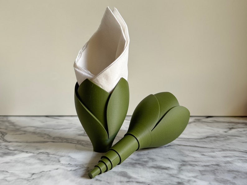 May include: Two green flower-shaped napkin holders. One holder has a white napkin inside.