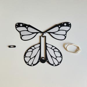 Può includere: Kit di artigianato di farfalla di carta nera con ali bianche, una corda e un piccolo pezzo di collegamento nero.