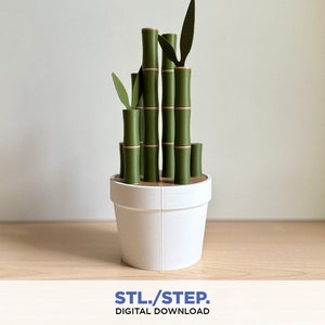 Könnte beinhalten: Ein 3D-gedrucktes Modell einer Topfpflanze mit Bambus. Die Pflanze besteht aus grünem und braunem Kunststoff und steht in einem weißen Topf. Der Topf steht auf einer Holzoberfläche.