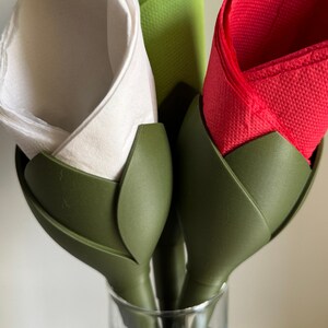 May include: Three napkin holders in the shape of green flower buds. Each holder has a different colored napkin inside: white, red, and green.