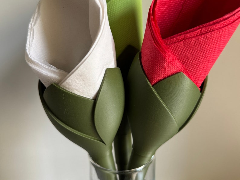 May include: Three napkin holders in the shape of green flower buds. Each holder has a different colored napkin inside: white, red, and green.
