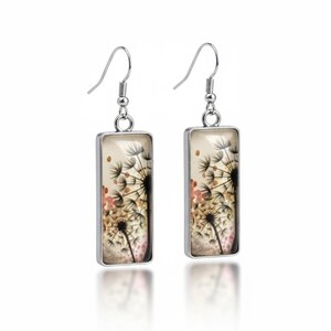 May include: A pair of rectangular silver earrings. Each earring displays a dandelion design with black seed heads, a tan background, and small pink accents. The earrings have a hook closure.