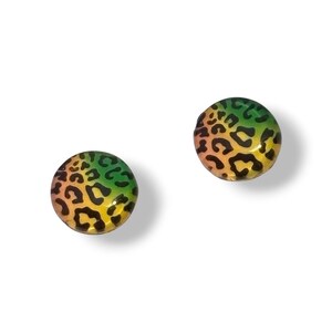 May include: A pair of round stud earrings with a leopard print pattern. The earrings display a colour gradient, shifting from green to yellow and orange, with black spots. The earrings are set against a white background.
