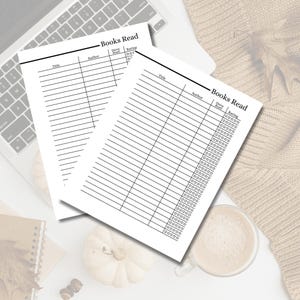 May include: Two white paper book trackers with the title "Books Read" printed at the top. Each sheet has columns for title, author, date read, and rating. The sheets are on a white surface with a laptop keyboard, a pumpkin, and a cup of coffee.