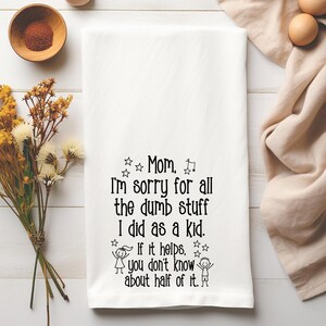 May include: White kitchen towel with black text that reads "Mom, I'm sorry for all the dumb stuff I did as a kid. If it helps, you don't know about half of it." The towel is surrounded by eggs, flowers, and a small bowl.