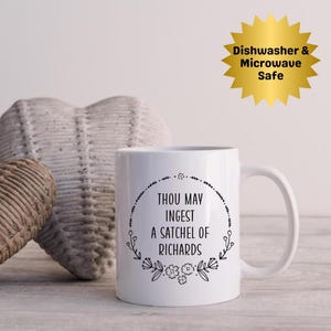 May include: White ceramic mug with a black floral wreath design and the text "THOU MAY INGEST A SATCHEL OF RICHARDS." A gold starburst graphic reads "Dishwasher & Microwave Safe."