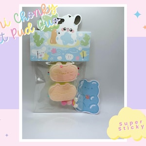 May include: A set of three mini cat pudding charms, featuring a blue gummy bear, a yellow cat with pink ears, and a yellow cat with pink ears and a pink nose. The charms are packaged in a clear plastic bag with a colourful card that says "Mini Chonky Cat Pud Chu" and "Super Sticky".
