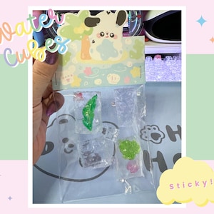 May include: A clear plastic bag containing decorative water cubes in various shapes, including a leaf and a small flower. The packaging features a cute cartoon design and the words "Water Cubes" in colourful lettering.