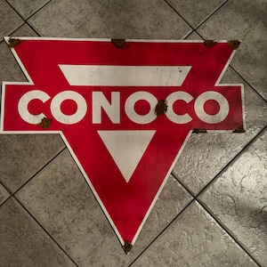 May include: A vintage Conoco gas station sign with a red triangle and white lettering. The sign is rusty and has a worn look.