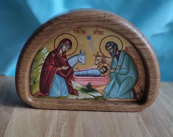 May include: A wooden, arched-top icon depicting a religious scene. The artwork features figures in robes, including a woman in a red cloak and a man in a blue robe, with text above. The icon is set against a light blue background.