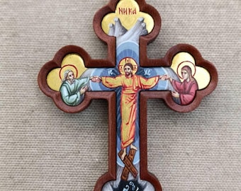 May include: Wooden Orthodox cross pendant with a detailed painted image of Jesus Christ. The cross has a dark brown frame with gold accents and a beaded necklace. The word "NIKA" is written in red at the top of the cross.